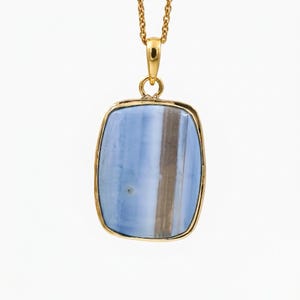 May include: A gold pendant necklace featuring a rectangular, smooth blue stone with a vertical brown band running through the center. The stone is encased in a polished gold frame and hangs from a delicate gold chain, creating a simple accessory.