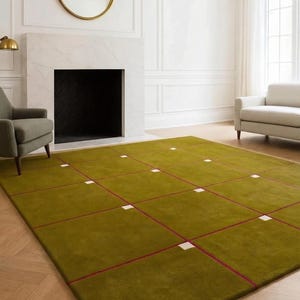 May include: A large rectangular area rug featuring a solid olive green surface divided by a grid of thin dark red lines. Small white square accents are positioned at the intersections of the grid lines across the entire rug surface.