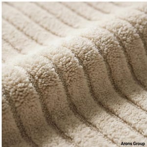 Può includere: Primo piano di un tessuto beige strutturato con un motivo a coste. Il tessuto ha un aspetto morbido e felpato, con creste visibili e una consistenza sfocata. Il materiale appare spesso e caldo, adatto per coperte o tappezzeria.