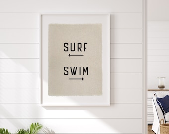 May include: A white framed print with the words "SURF" and "SWIM" with arrows pointing in opposite directions. The print is hanging on a white shiplap wall.