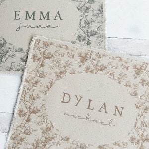 May include: Two personalized placemats with a toile pattern. The top placemat is green and white with the name "EMMA" and the word "june" written in cursive. The bottom placemat is brown and white with the name "DYLAN" and the word "michael" written in cursive.