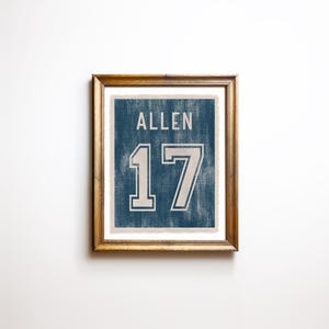 May include: Framed print featuring the name "ALLEN" above the number "17" in a vintage style. The text and numbers are white against a blue background, with a distressed texture. The frame is a warm brown color.
