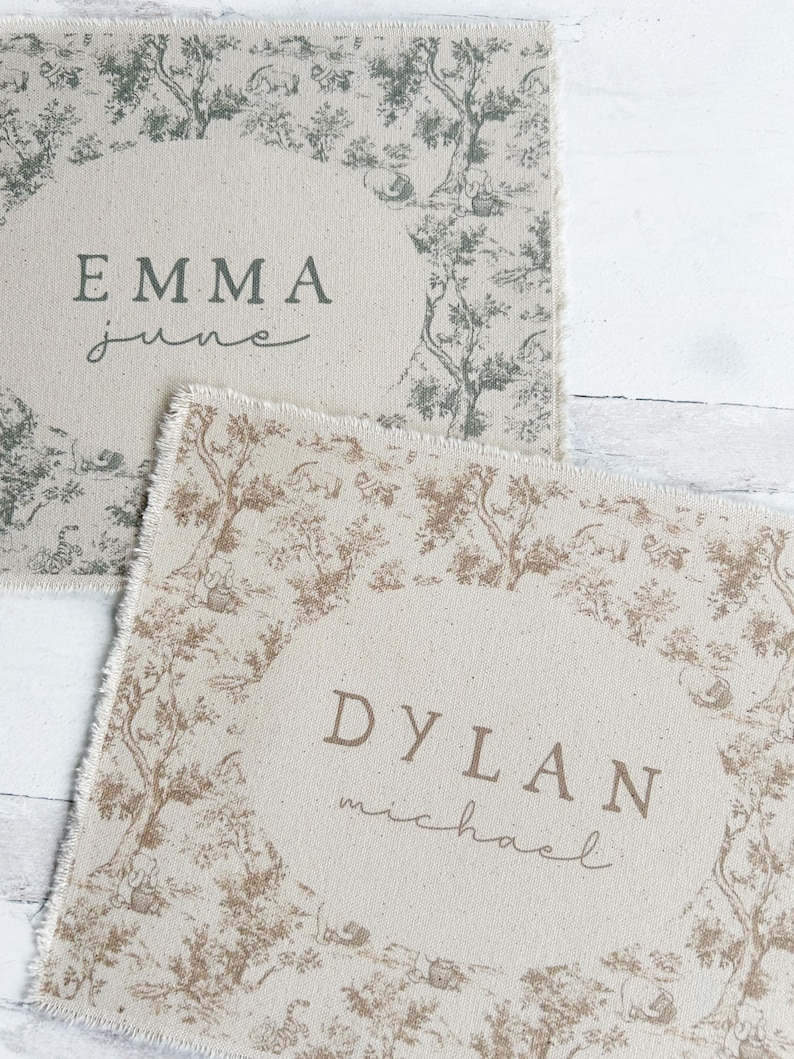 May include: Two personalized placemats with a toile pattern. The top placemat is green and white with the name "EMMA" and the word "june" written in cursive. The bottom placemat is brown and white with the name "DYLAN" and the word "michael" written in cursive.