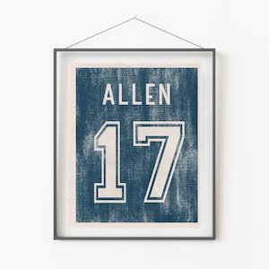 May include: Framed print featuring a distressed navy blue background with the name "ALLEN" and the number "17" in white. The print is encased in a black frame and hangs against a white wall.