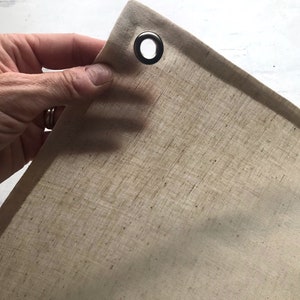 Puede incluir: Primer plano de una tela beige natural con un ojal de metal. La tela es texturizada y tiene un brillo sutil.