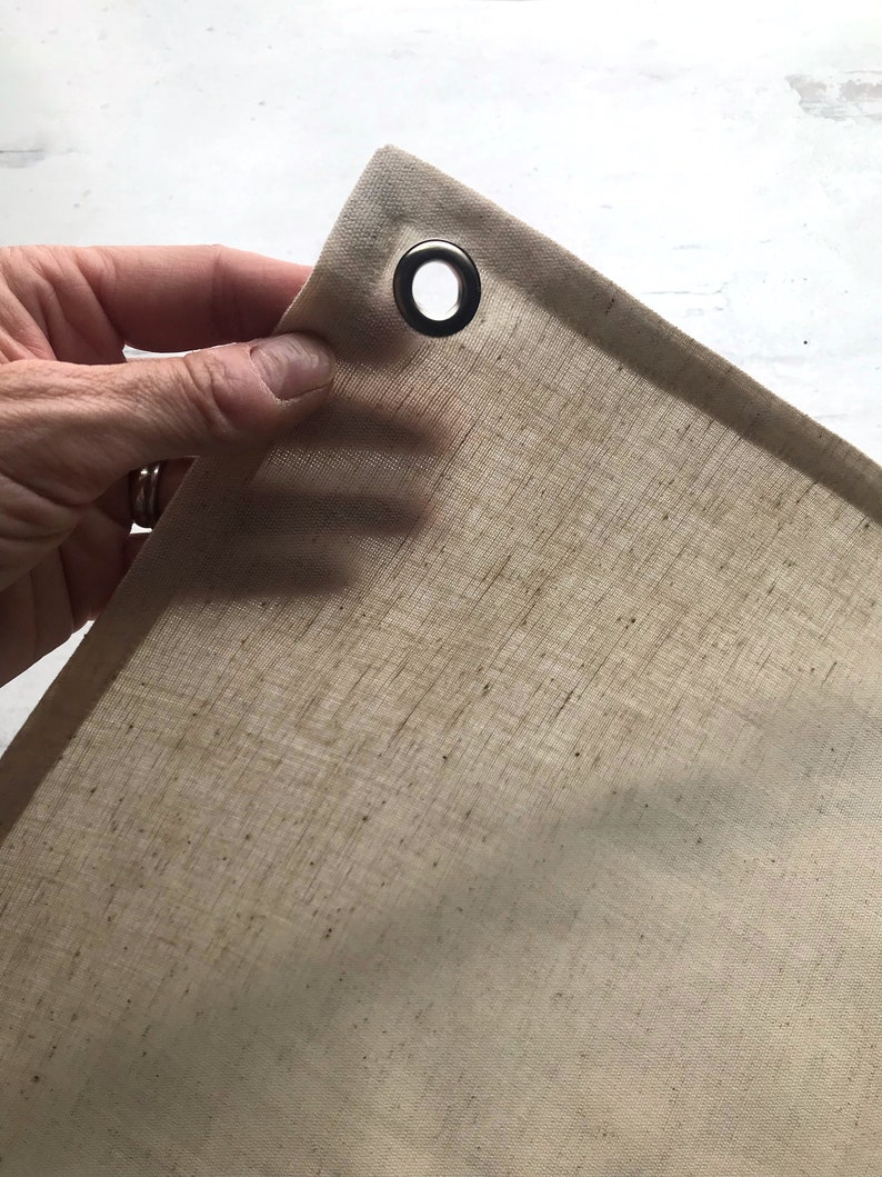Puede incluir: Primer plano de una tela beige natural con un ojal de metal. La tela es texturizada y tiene un brillo sutil.