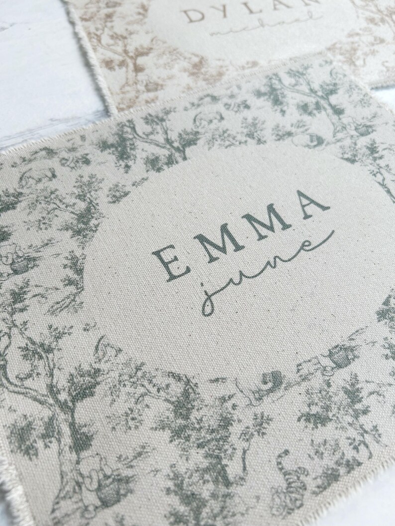 May include: A beige fabric with a green toile pattern and the name "EMMA june" printed in black.