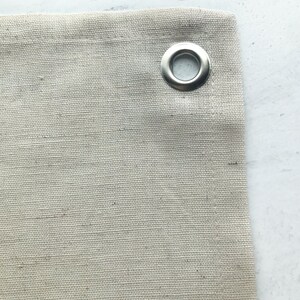 Puede incluir: Primer plano de una tela de lona beige con un ojal de metal plateado.