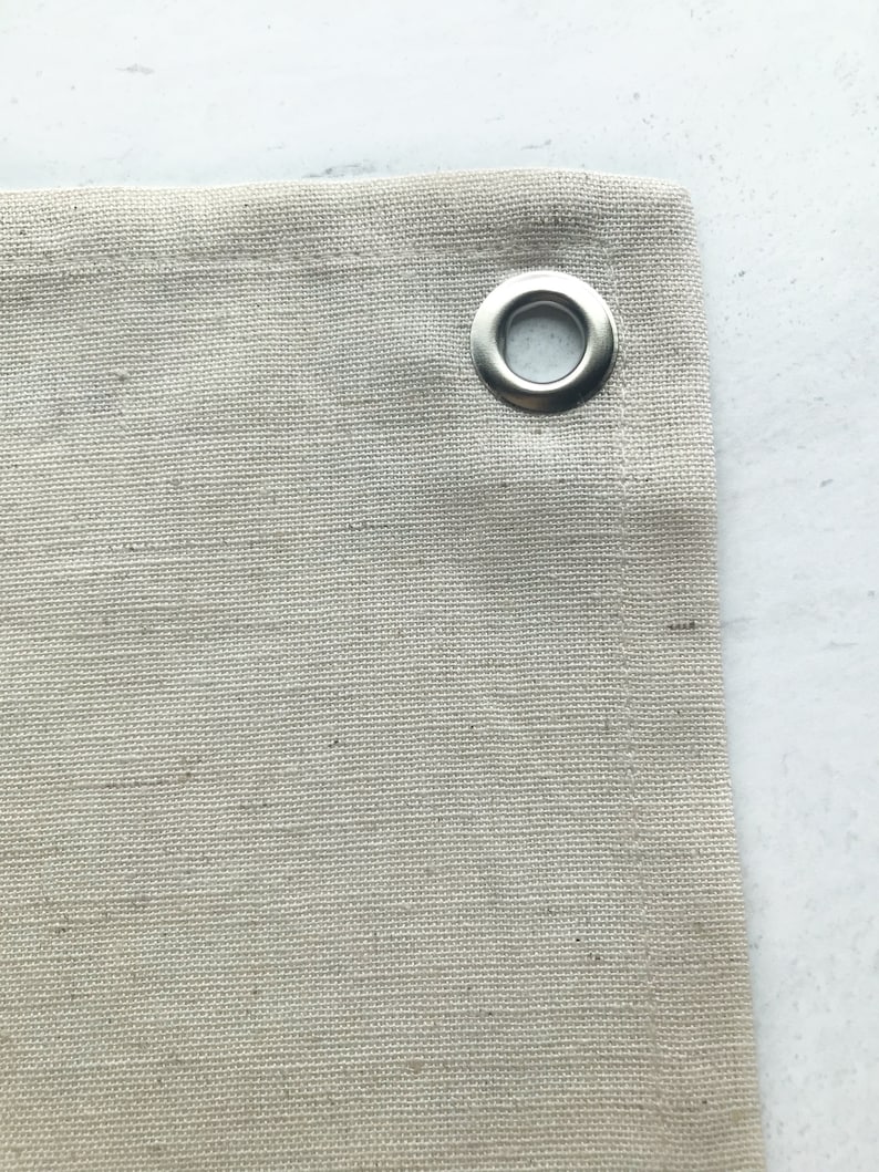 Puede incluir: Primer plano de una tela de lona beige con un ojal de metal plateado.