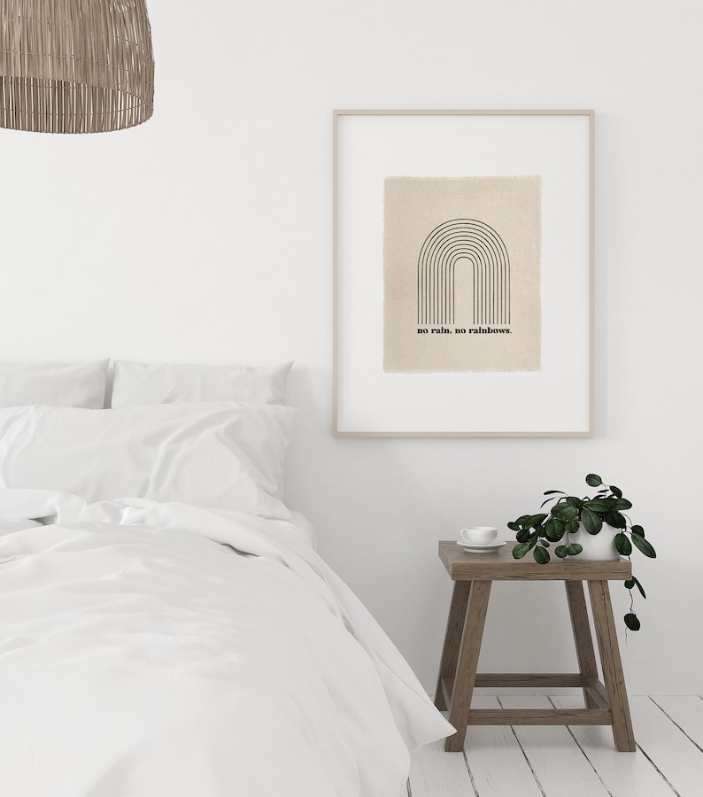 May include: A framed print with a black and white illustration of a rainbow with the text "no rain, no rainbows." The print is hanging on a white wall above a wooden nightstand with a potted plant and a white cup.