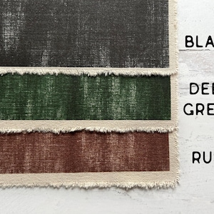 May include: Three fabric swatches in black, deep green, and rust. Each swatch has a distressed, textured appearance and a frayed edge. The words "BLACK", "DEEP GREEN", and "RUST" are printed in black.