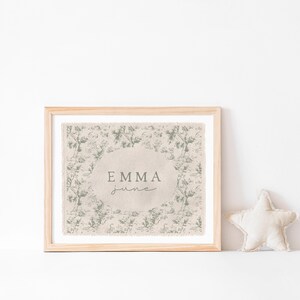May include: A framed print with a beige background and a green floral pattern. The print has the name "Emma June" in a cursive font.