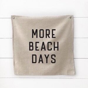 Puede incluir: Una pancarta de lona beige con el texto "MORE BEACH DAYS" impreso en negro.