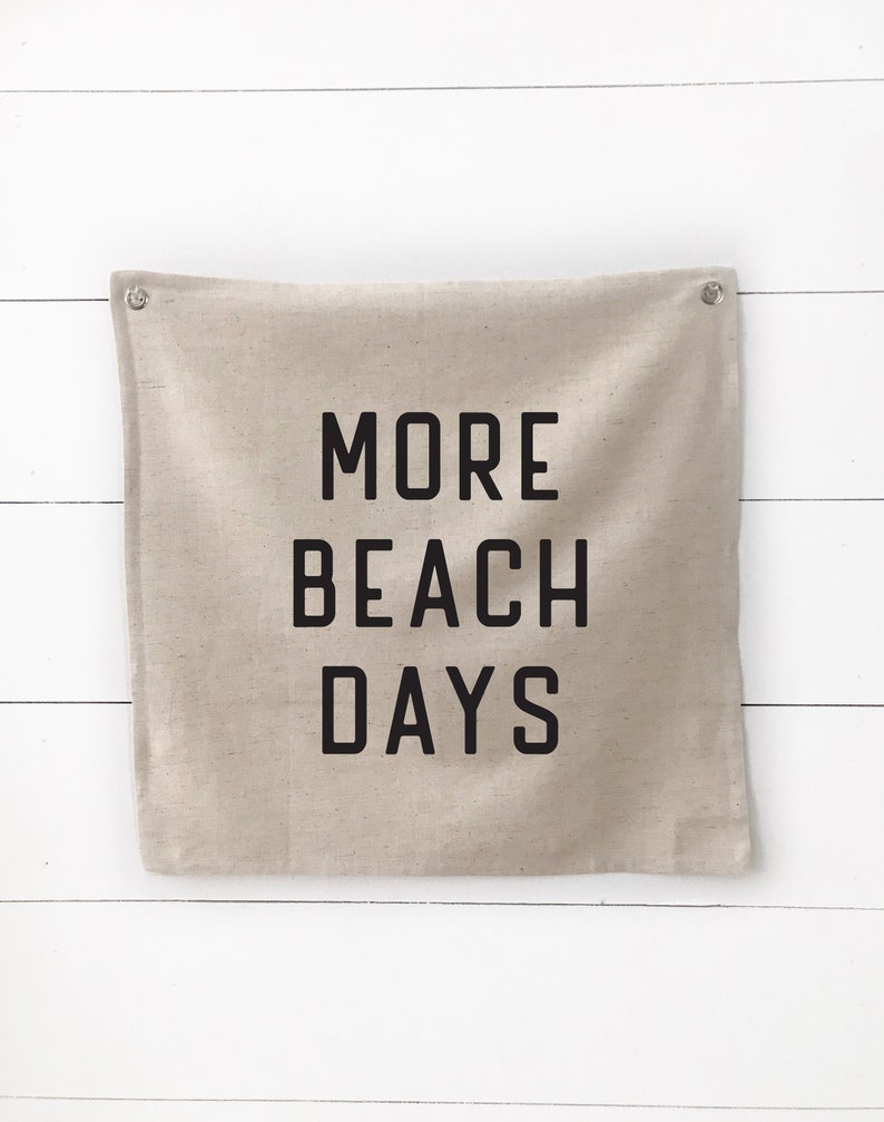 Puede incluir: Una pancarta de lona beige con el texto "MORE BEACH DAYS" impreso en negro.