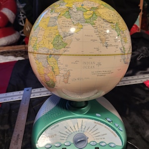 May include: A detailed, interactive globe with a light green base and a beige sphere displaying world geography. The base features buttons and a stylus, with text indicating various learning functions. The globe is approximately 12 inches in height.
