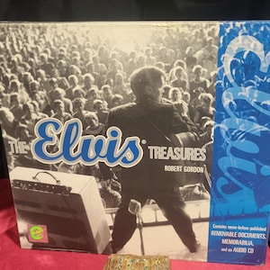 May include: A box set titled "The Elvis Treasures" by Robert Gordon. The box features a black and white image of Elvis Presley performing on stage in front of a crowd. The box also includes text that says "Contains never-before-published REMOVABLE DOCUMENTS, MEMORABILIA, and an AUDIO CD."