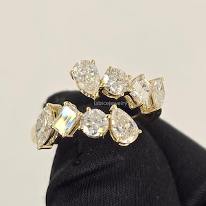 Può includere: Un anello aperto in oro con una serie di pietre preziose trasparenti di varie forme, tra cui taglio a goccia, rotondo, marquise e smeraldo, disposte su due file. Il testo labicejewelry è visibile al centro del design dell'anello.