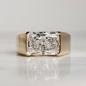 Op de afbeelding: Een gouden ring met een grote, rechthoekige, gefacetteerde heldere edelsteen in een gladde, brede zetting. De band heeft een gepolijste afwerking en een solide, dikke constructie. De tekst labicejewelry is zichtbaar aan de zijkant van de zetting.