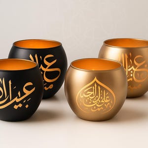 Peut inclure: Quatre bougeoirs décoratifs noirs et dorés. Chaque bougeoir a une forme arrondie avec un intérieur doré. De la calligraphie arabe dorée est présente à l'extérieur de chaque bougeoir. Les bougeoirs sont sur une surface blanche.
