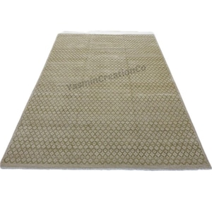 May include: A rectangular rug with a repeating floral pattern in shades of beige and olive green. The rug has a fringe on one end and a textured surface. The rug is suitable for a living room or bedroom.