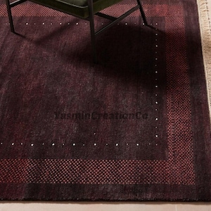 Op de afbeelding: Een diepbordeauxrood vloerkleed met een donker centraal veld en een subtiele rand van kleine witte stippen. Het kleed heeft een bredere buitenrand met een gestructureerd, herhalend patroon in een lichtere rode tint en franjes. Tekst YasminCreationCo.