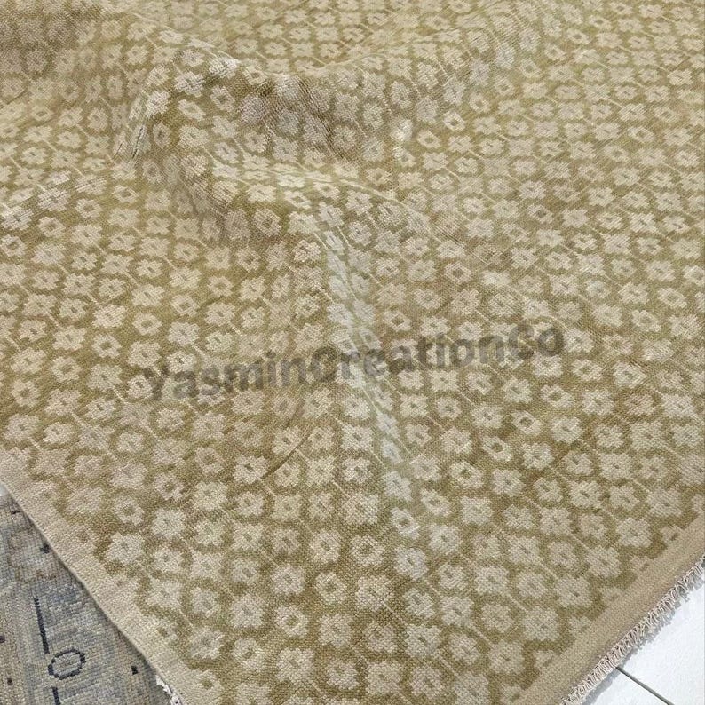 May include: Close-up of a beige rug with a repeating floral pattern. The rug has a textured surface and a fringe along one edge. The text "yasminCreationCo" is visible on the rug.
