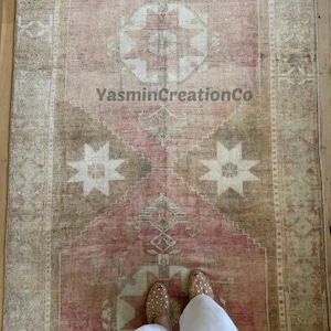 May include: A vintage-style rug in shades of pink, beige, and brown, featuring geometric star and diamond patterns. The rug has a distressed look, with the text "YasminCreationCo" visible. The rug is rectangular and appears to be on a wooden floor.
