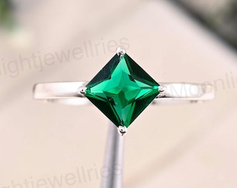 May include: A silver ring featuring a square-cut, vibrant green gemstone. The gemstone is the focal point, set in a simple, elegant band. The ring's design is minimalist, highlighting the gemstone's color and shape.