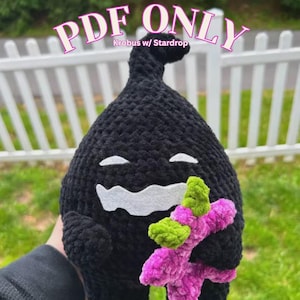 May include: A handmade black crochet plushie with a white felt mouth and eyes, holding a pink and green crochet star. The text "PDF ONLY" and "Krobus w/ Stardrop" are visible in the image.