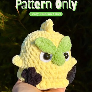 May include: A crocheted chick in yellow with a green unibrow and black feet. The chick has large, round eyes and is labelled "Pattern Only" with "Leafy Unibrow Chick" below. The background is blurred green foliage.