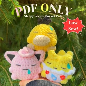 以下が含まれることがあります： 黄色とピンク色の、目が閉じて涙を流している3つの編みぐるみのぬいぐるみ。「PDF ONLY」と「Sleepy Series: Pocket Pals」の文字が見える。赤い星には「Low Sew!」と書かれている。おもちゃは緑色の背景の前に持たれている。