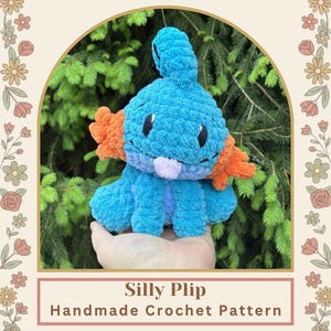 May include: A handmade crochet plush toy in shades of blue and orange, resembling a cartoon creature. The toy has a rounded body, small arms, and a tail. The text "Silly Plip Handmade Crochet Pattern" is displayed below the toy.