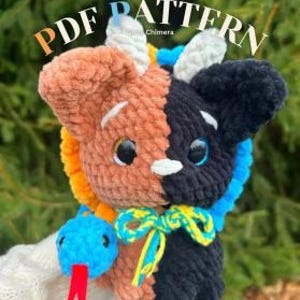 May include: A handmade crochet plushie in the shape of a split-faced creature, with one side brown and the other black. It has large, round eyes, a yellow and blue bow, and a small blue snake with a red tongue. The text "PDF PATTERN" is visible.