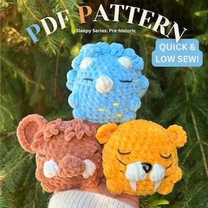May include: Three handmade crochet dinosaur plushies in blue, brown, and orange. The blue dinosaur has white accents, the brown has large ears, and the orange has large fangs. The image includes the text "PDF PATTERN" and "QUICK & LOW SEW!"