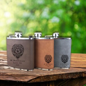 May include: Three stainless steel flasks with leather-like covers in brown, tan, and gray. Each flask features a police badge design and the text "POLICE OFFICER", along with a name, class, and year.