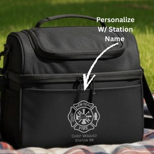 May include: Black insulated lunch bag with a top handle, shoulder strap, and front pocket. Features a white New York Fire Department emblem and text that reads "Personalize W/ Station Name".