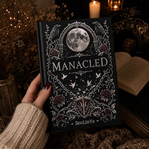Op de afbeelding: Een hardcover boek met een zwarte kaft met de titel "MANACLED" in witte letters. Het ontwerp van de kaft omvat een volle maan, raven, rozen en een schildembleem. De naam van de auteur, SenLinYu, staat onderaan.