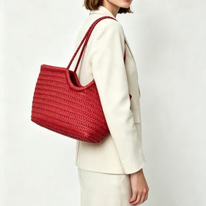 Könnte beinhalten: Eine leuchtend rote Tragetasche mit einer detaillierten geflochtenen Textur auf der gesamten Außenseite. Die Tasche verfügt über zwei dünne, geflochtene Schulterriemen und ein strukturiertes Design mit offener Oberseite und geschwungener Silhouette.