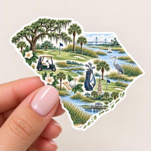 May include: A die-cut sticker shaped like the state of South Carolina featuring a detailed illustration of a golf course, a golf cart, a golf bag with clubs, a golf ball, a heron, palm trees, a bridge, and white magnolia flowers.