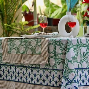 Op de afbeelding: Een groen en wit bloemenpatroon tafelkleed met een blauw en wit geschulpte rand. De tafel is gedekt met wijnglazen, een witte vaas en een boeket rode en witte bloemen. Het tafelkleed is gemaakt van een zacht, comfortabel materiaal.