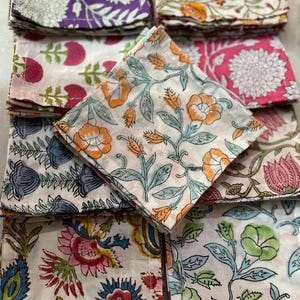 Puede incluir: Una colección de servilletas de tela plegadas con estampados florales. Las servilletas presentan varios diseños en colores como morado, naranja, rosa, azul y verde. Los estampados florales incluyen flores y hojas.