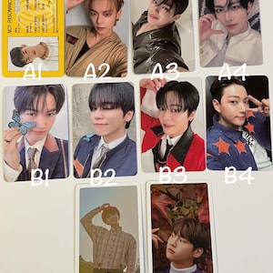 May include: A collection of K-pop idol photo cards featuring various members. The cards display individual portraits of the idols in different poses and outfits. Some cards have text and design elements, including the group's name and member information.