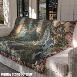 May include: A woven throw blanket measuring 50 inches by 60 inches, featuring a detailed forest scene with a white stag, flowing water, and floral elements in shades of green, brown, and cream, finished with a decorative fringed edge.