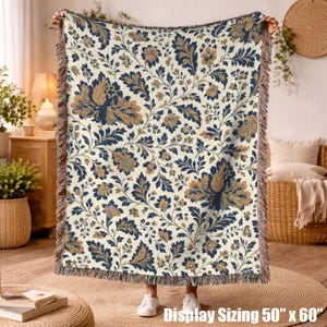 May include: A woven throw blanket featuring a cream background with a repeating floral and leaf pattern in navy blue and tan. The blanket has a fringed edge and measures 50 inches by 60 inches as indicated by the printed text.