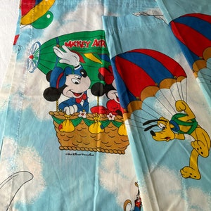 May include: A pair of blue and white curtains featuring Mickey Mouse, Minnie Mouse, and Pluto in a hot air balloon. The balloon is labeled "Mickey Air" and the curtains have a white background with clouds.