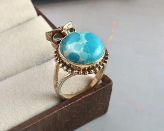 May include: A gold-toned ring featuring a large, round, mottled turquoise-colored stone set in a bezel. The ring design incorporates an owl motif at the top, with two small, light blue circular stones serving as eyes above the main turquoise stone.