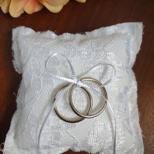 May include: White lace ring pillow with two silver wedding bands tied with a white satin ribbon.