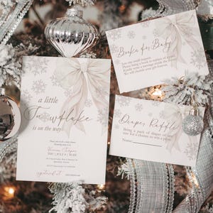 May include: Baby shower invitations and cards with snowflake and bow designs. The invitations read "a little snowflake is on the way" and include event details. Cards request books and diaper raffle participation. The decorations include silver ornaments and ribbon.