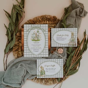 May include: Baby shower invitation set with a bunny theme. The set includes an invitation, a "Books for Baby" card, and a "Diaper Raffle" card. The cards have a gingham pattern and illustrations of bunnies and flowers. Greenery and a woven mat are in the background.