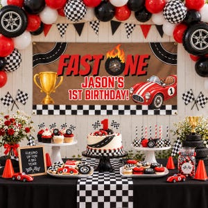 May include: A race car themed birthday party display featuring a banner with the text FAST ONE JASON'S 1ST BIRTHDAY, a cake with a number one topper, cupcakes, cookies, cake pops, a gold trophy, and a black and white checkered tablecloth.